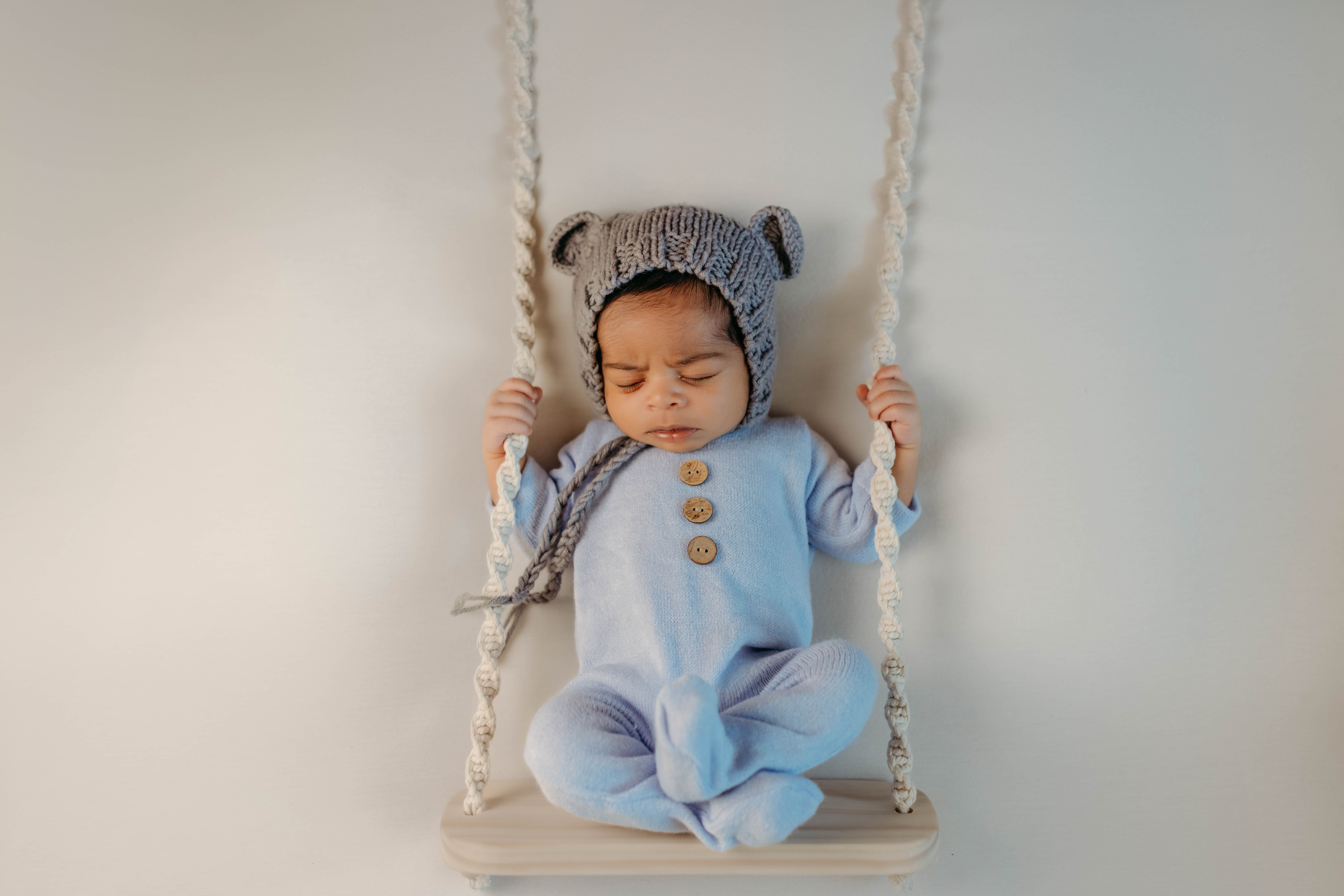 Newborn baby boy posed on a swing with teddy bear bonnet
