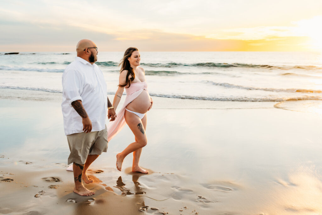 beach maternity session with couple walking down the beach at sunset in San Diego California