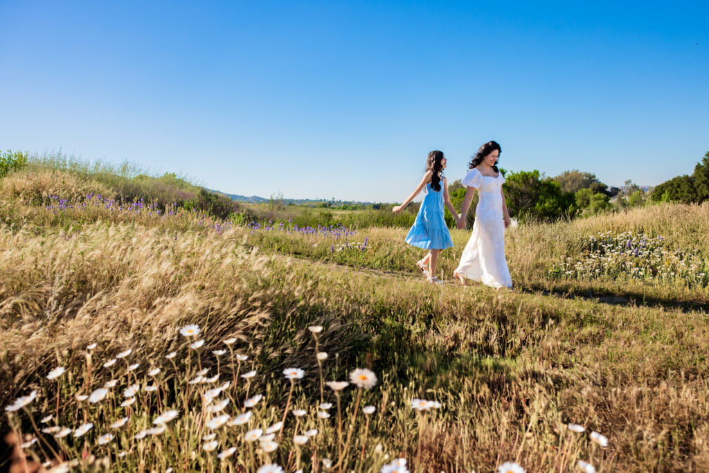 mother and daughter walking together holding hands through a field in Murrieta California